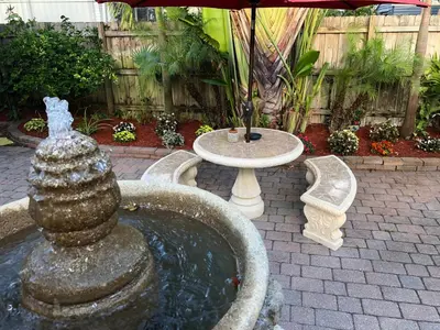 a fountain in a garden with a table and an umbrella at Calypso Inn Wilton Gay Male Resort in Fort Lauderdale