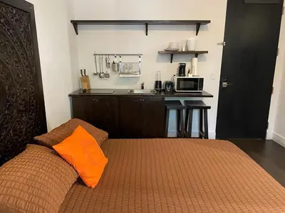 a bedroom with a bed with an orange pillow and a kitchen at Vive Zen Queen Room in Miami