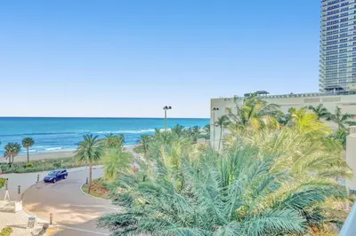 a view of the beach and palm trees from a balcony at Oceanfront Condo Direct Ocean & Beach Club Access in Hollywood