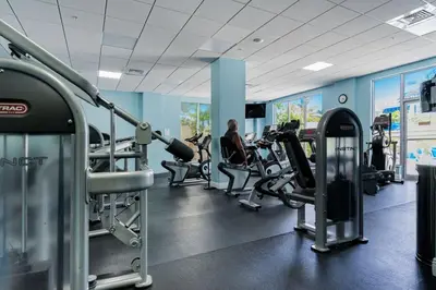 a gym with cardio equipment and a woman in the background at Ocean View Modern Condo Beach Access 11M in Hollywood