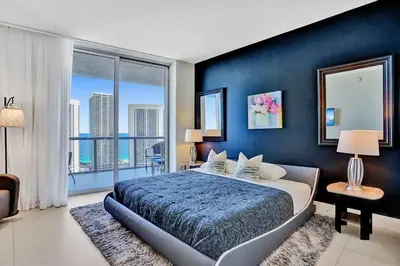 a bedroom with a large bed with a blue wall at Sky-High Spacious Ocean View Condo 4 BDRS 3 BATH in Hallandale Beach