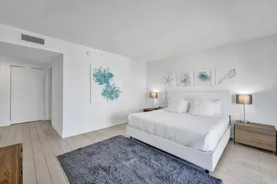 a white bedroom with a large white bed and a table at Modern Ocean View 3 Bedroom Condo Resort Amenities in Hallandale Beach