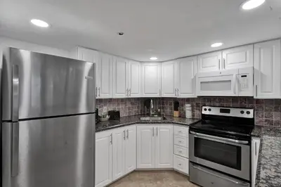 a kitchen with white cabinets and a stainless steel refrigerator at Modern Miami Beach Condo with Beach Service & Pool in Miami Beach
