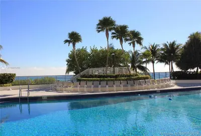 a large swimming pool with palm trees and the ocean at Apartamento en Miami Beach sobre la playa in Miami Beach