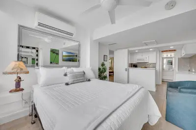 a white bedroom with a large bed and a kitchen at Retreat by Beach Waterfront Lago Key in Fort Lauderdale