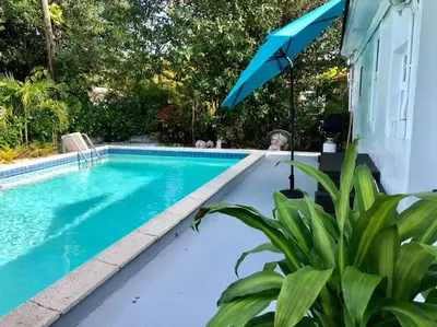a swimming pool with a blue umbrella next to a house at HOUSE WITH POOL, 10 MINS DRIVE TO THE BEACH! in Miami Shores