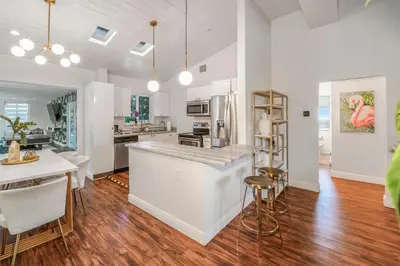 a kitchen and dining room with white walls and wood floors at La Playita 4-BR Heated Pool Miami 16 Guests in Miami