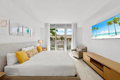 a white bedroom with a bed and a large window at Water View Building With Pool - 5-Min Walk To The Beach in Hallandale Beach