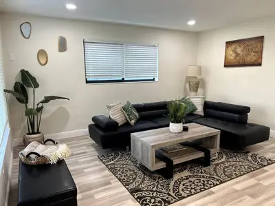 a living room with a black couch and a table at Modern Tropical Oasis with Arcade, HotTub & MiniGolf in Hollywood