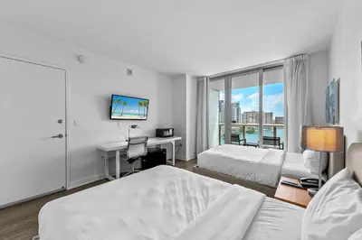 a bedroom with two beds and a desk and a window at Water View Building With Pool - 5-Min Walk To The Beach - Cozy Studios in Hallandale Beach