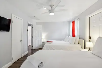 a white bedroom with two beds and a flat screen tv at Patio and Yard Family-Friendly Miami Oasis! in Miami Gardens