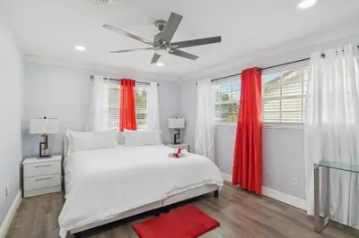 a white bedroom with a white bed and red curtains at Patio and Yard Family-Friendly Miami Oasis! in Miami Gardens