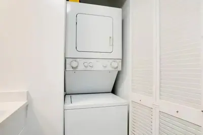 a small white refrigerator in a white kitchen at Chic Penthouse: 3BR x Pool x Gym x 2 Parking Spots in Miami