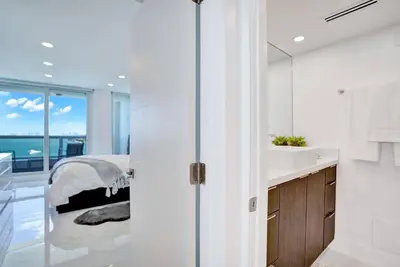 a white bedroom with a bed and a bathroom at Feels Like Summer ~ Panoramic Water Views! in Miami