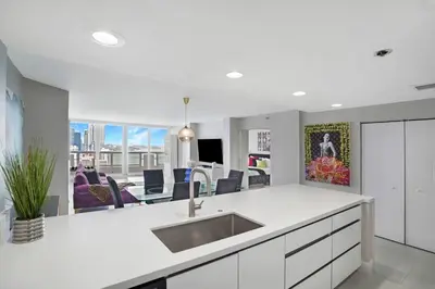a white kitchen with a sink and a living room at Higher Love! Water Views and Cool Vibes in Miami