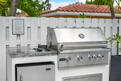 a barbecue grill with a fence in front of a house at Seashell Walk To The Beach Comfy Beds Firepit Pool in Fort Lauderdale
