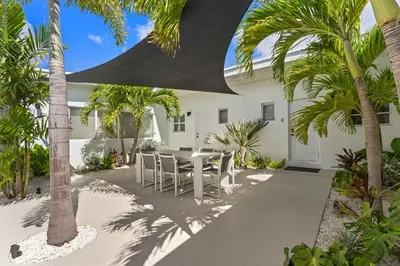 a patio with a table and chairs and palm trees at The Sandbar Walk To Beach Comfy Beds Firepit Pool in Fort Lauderdale