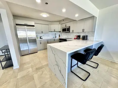 a kitchen with a white counter and two black chairs at Oceanfront Haven Retreat Beach Service 502 in Miami Beach