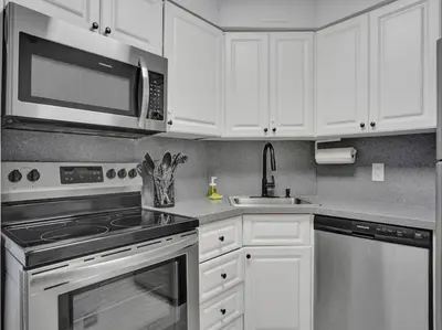a kitchen with white cabinets and a stove and a microwave at High Floor Beachfront Condo Beach Service 1509 in Miami Beach