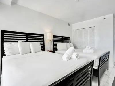a white bedroom with two beds with white pillows at Lovely Ocean View Condo Beach Service 704 in Miami Beach