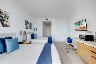 a bedroom with two beds and a desk with a tv at Upper studio w Balcony Pool Gym Near Beach in Hallandale Beach
