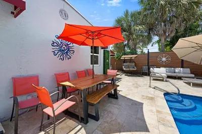 a patio with a wooden table with a red umbrella at Palms Retreat! Giant Heated Pool-HotTub-FirePit-5Min2Beach-Pets-EV Chgr in Fort Lauderdale