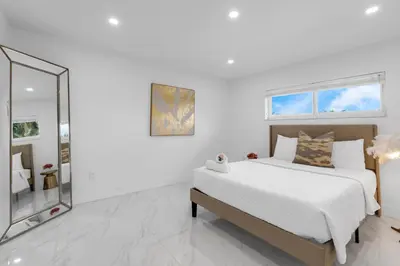 a white bedroom with a bed and a mirror at MIA MANSION W/ POOL / BBQ /CABANNA / OUTDOOR BAR in Tamiami