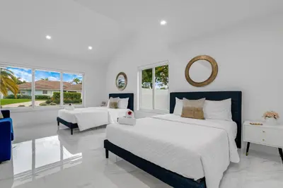 a white bedroom with two beds and a mirror at MIA MANSION W/ POOL / BBQ /CABANNA / OUTDOOR BAR in Tamiami