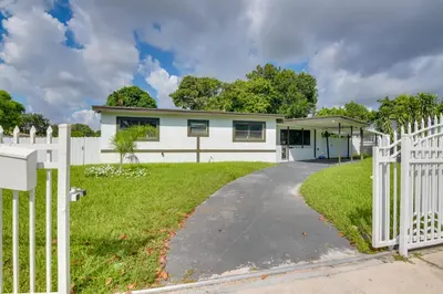 a house with a white fence and a driveway at Luxe Miami Home Outdoor Kitchen, Gas Grill! in Miami Gardens