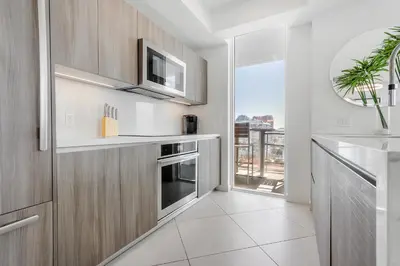 a kitchen with wooden cabinets and a microwave and a window at Tiffany Hazel - Rooftop Pool, Gym, & Walk to Beach in Fort Lauderdale