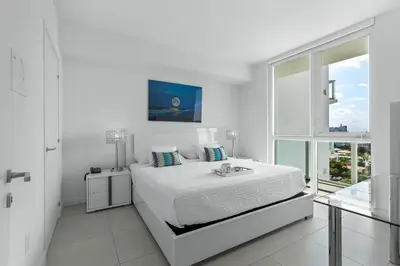a white bedroom with a bed and a window at Tiffany Ebony - Ocean & Canal views, Walk to Beach in Fort Lauderdale