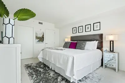 a white bedroom with a large bed and a plant at Tiffany Sage - Rooftop Pool, Gym, & Walk to Beach in Fort Lauderdale