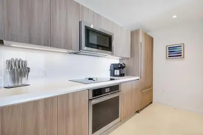 a kitchen with wooden cabinets and a tv on the wall at Tiffany Indigo - Rooftop Pool, Gym, Walk to Beach in Fort Lauderdale
