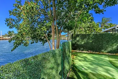 a fence with a tree next to the water at Renovated professional design, grill lake view! in Hallandale Beach