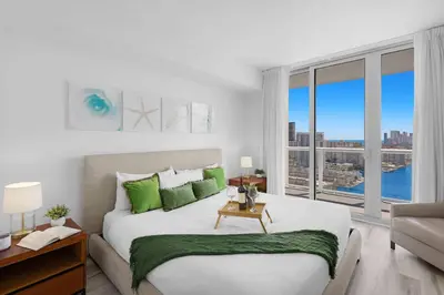a white bedroom with a large bed with green pillows at Near Beach - Pool - Infinity View - Balcony - Gym in Hallandale Beach