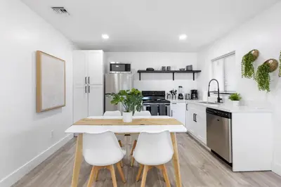 a white kitchen with a wooden table and white chairs at Sun Getaway Rentals in Fort Lauderdale