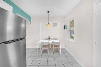 a white kitchen with a table and a refrigerator at Bluewave Bungalow - #1 Charming & Comfortable 2 1 in Dania Beach
