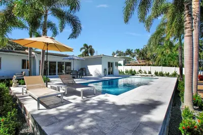 a pool with chairs and an umbrella next to a house at Lakefront Family Fun Home with Private Dock 3BR 2B in Fort Lauderdale