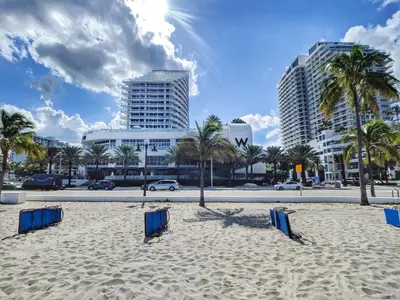 a beach with chairs and palm trees and buildings at WVR Vacation Residences 709 in Fort Lauderdale