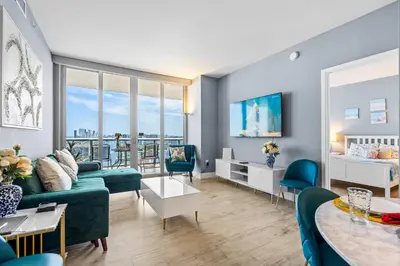 a living room with blue furniture and a large window at Ocean Views - Pool & Gym - Pet Friendly - Close to Beach in Hallandale Beach