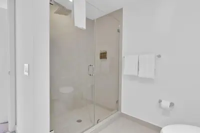 a white bathroom with a shower and a toilet at Beachfront Escape Pool Gym Stunning Views 30th floor in Hallandale Beach