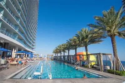 a pool on the beach with palm trees and a hotel at LYFE on the Beach 25th floor 1 bed unit with Oceanview in Hollywood