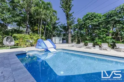 a swimming pool with two blue chairs and trees at Cascada-Luxe Resort Heated Pool HotTub Wlk 2 Beach in Fort Lauderdale