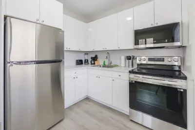 a kitchen with white cabinets and a stainless steel refrigerator at Prime Location Apt on Calle Ocho in Little Havana in Miami