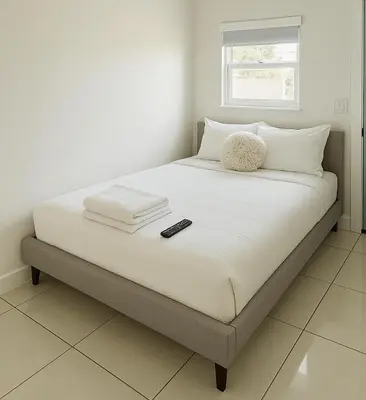 a bed with white sheets and a remote control on it at Modern Home - Termpurpedic Queen bed, Laundry, Free Parkging, EV Tesla in Hollywood