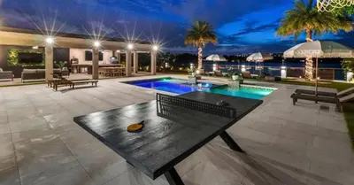 a patio with a table and a pool at night at Waterfront Mansion The GlamHomes in North Miami Beach
