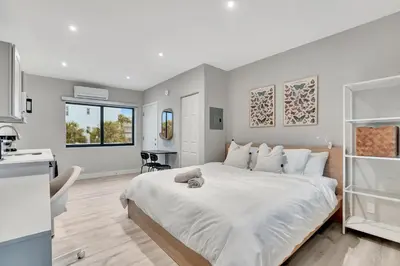 a bedroom with a large white bed and a kitchen at 2 Condo Combo - Walk to Beach Off Las Olas 1AB in Fort Lauderdale