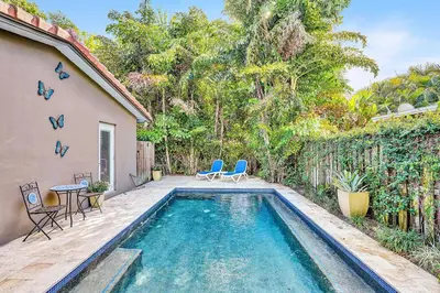a swimming pool with two chairs and a table next to a house at Heated pool, parking, 5 min walk to food and fun! in Fort Lauderdale