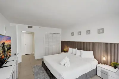a bedroom with a large white bed and a flat screen tv at Oceanfront condo beach service 411 in Miami Beach