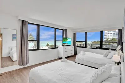 a white bedroom with two beds and a television at Spacious Ocean View Resort Beach Condo 601 in Miami Beach